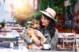 jolie jeune femme assise dans un café, se détendre et tenant son chien. cafétéria acceptant les animaux domestiques, belle fille avec son chien assis dans un café et buvant du café. photo