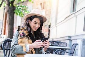 jeune femme avec son chien dans une cafétéria acceptant les animaux. jeune femme envoyant des SMS sur son téléphone portable tout en se relaxant au café pendant son temps libre avec son chien