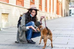 jeune femme aux cheveux longs et masque de protection du visage embrassant un chien drôle dans la rue pendant l'isolement de la pandémie de coronavirus. jeune femme souriante profitant d'une bonne journée et posant avec un animal de compagnie. photo