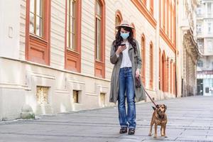 femme pendant l'isolement pandémique marchant avec son chien et utilisant un téléphone portable dans la rue. photo