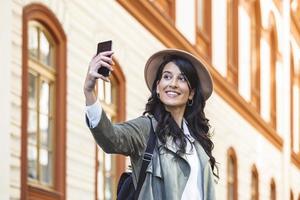 touriste posant pour un selfie dans une rue. vlogger enregistrant du contenu pour son vlog de voyage. jolie jeune fille souriante fait selfie sur un appareil photo tout en marchant à l'extérieur.