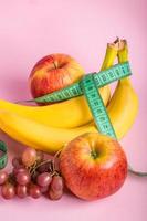 fruits frais et ruban à mesurer sur fond rose. le concept de régime alimentaire et d'alimentation saine. photo