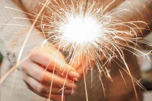 Célébration du nouvel an. jeune femme tient un cierge magique dans ses mains. nuit de Noël. brillantes étincelles de feu. photo