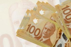 100 billets de dollars canadiens sont empilés sur fond de gros billets de banque semi-transparents. présentation abstraite de la monnaie nationale photo