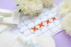 serviettes et tampons menstruels sur le calendrier de la période de menstruation avec des fleurs blanches sur fond lilas photo