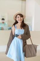 femme asiatique en robe bleue et chapeau se sentant heureuse en souriant et en regardant la caméra photo