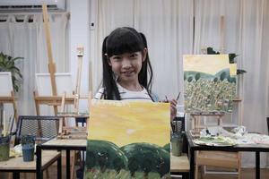 une étudiante asiatique montre son travail de peinture, fière d'un portfolio, d'une image couleur acrylique sur toile dans une salle de classe d'art et d'un apprentissage créatif avec des compétences de talent dans l'enseignement en studio de l'école primaire. photo