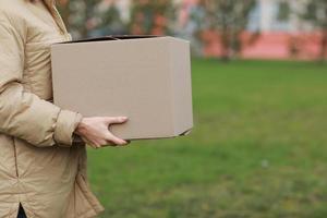 une fille de livraison recadrée tient une boîte en carton vide à l'extérieur sur un fond de complexe résidentiel. service coronavirus. shopping en ligne. maquette. photo