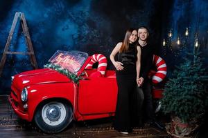 jeune couple heureux homme et femme amoureux à noël se serrent dans leurs bras près d'une voiture rétro rouge avec des cadeaux du nouvel an. baiser, fille, bonheur, célébration de noël en quarantaine, vacances. photo
