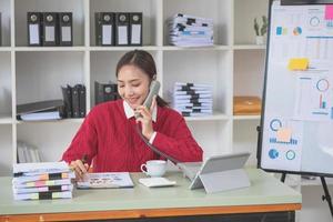 femme d'affaires tenant un téléphone parlant à son superviseur et montrant ses données de profit dans des graphiques à son superviseur à l'aide d'un ordinateur portable. photo