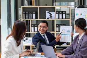 une équipe d'hommes d'affaires planifient leurs bénéfices avec leurs ordinateurs portables et leurs graphiques et utilisent une calculatrice pour calculer le solde annuel de leur entreprise. photo