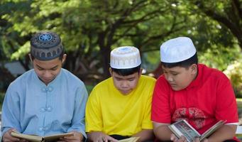 un groupe de garçons musulmans s'assoient ensemble sous l'arbre dans le parc de l'école, ils lisent, apprennent, parlent, suggèrent et consultent les problèmes d'apprentissage les uns aux autres, mise au point douce et sélective. photo