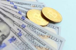bitcoins dorés et billets de cent dollars se trouvent sur fond bleu clair photo
