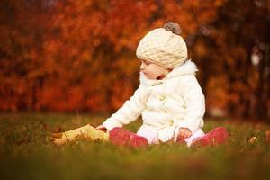 belle petite fille assise avec une grande feuille au parc d'automne photo