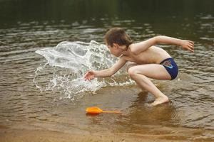 un garçon s'amuse à jouer avec un jet d'eau dans la rivière en été. copie espace photo