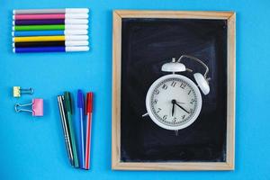 tableau scolaire et accessoires de papeterie, crayons, réveil et stylos sur fond bleu. concept de retour à l'école. photo