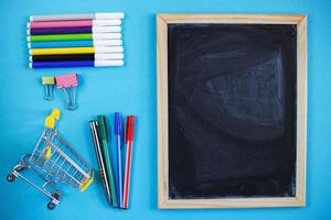 tableau d'école et accessoires de papeterie, crayons, stylos, panier sur fond bleu. concept de retour à l'école. photo