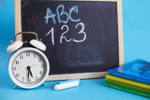 manuels scolaires et réveil avec tableau d'école sur fond bleu. retour à l'école. concept d'éducation ou d'entreprise photo