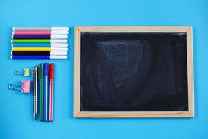 tableau d'école et accessoires de papeterie, crayons et stylos sur fond bleu. concept de retour à l'école, vue de dessus. photo