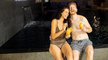 jeune couple se détendre et boire du jus d'orange au bord de la piscine photo