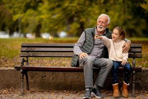 grand-père passe du temps avec sa petite-fille sur un banc dans le parc le jour de l'automne