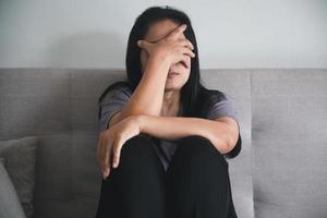 schizophrénie avec concept de dépression solitaire et triste en santé mentale. femme déprimée assise sur le canapé à la maison avec une pièce sombre se sentant misérable. les femmes sont déprimées, craintives et malheureuses. photo