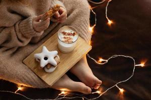 les pieds et les mains nus de l'enfant tiennent un biscuit de pain d'épice un verre de lait de poule, des bonbons de noël des biscuits au gingembre. photo