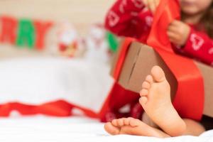 enfants pieds nus se bouchent. ambiance festive. concept de noël, vacances. bonne année. mise au point sélective. enfant fille assise sur le lit tenant un cadeau de noël ouvert. concept d'hiver du matin du nouvel an photo