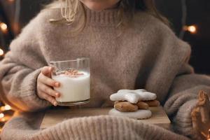 les pieds et les mains nus de l'enfant tiennent un biscuit de pain d'épice un verre de lait de poule, des bonbons de noël des biscuits au gingembre. photo