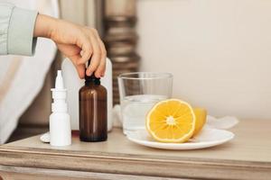 la main de l'enfant en gros plan prend des médicaments dans une bouteille. médicaments de santé sur la table de chevet. bouteilles de maquette gouttes et spray.enfant malade dans un lit photo