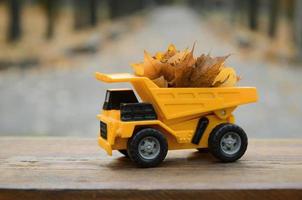 le concept de récolte saisonnière des feuilles mortes d'automne est représenté sous la forme d'un camion jouet jaune chargé de feuilles sur fond de parc d'automne photo