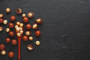 noix de macadamia décortiquées et noix de macadamia pelées sur fond noir texturé dans une cuillère en bois. faible contraste photo