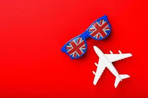 un avion de passagers blanc vole dans des lunettes de soleil avec le drapeau du royaume-uni, sur fond rouge. photo