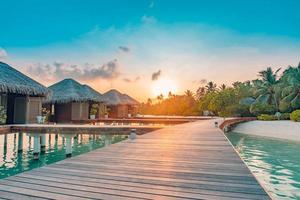 coucher de soleil sur l'île des maldives, complexe de villas sur l'eau de luxe et jetée en bois. beau ciel et nuages et fond de plage pour les vacances d'été et le concept de voyage photo