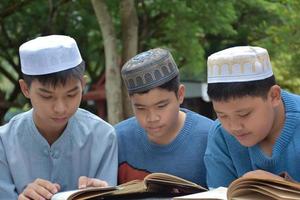 jeunes garçons asiatiques musulmans ou islamiques assis ensemble dans le parc de l'école pour lire, apprendre, faire et consulter les devoirs et attendre d'apprendre des sujets religieux à l'école, mise au point douce et sélective. photo