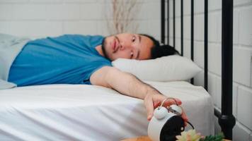 jeune homme asiatique se réveille le matin, un homme asiatique éteint le réveil après s'être réveillé sur le lit dans la chambre à la maison. beaux hommes sieste, somnolent se détendre dans le concept de maison moderne. photo