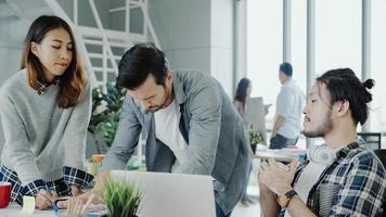 Groupe de gens d'affaires habillés avec désinvolture discutant d'idées dans des vêtements décontractés intelligents travaillant sur un ordinateur portable alors qu'il était assis sur le bureau pendant que son gestionnaire en colère se tenait en colère, jetant des papiers sur le bureau. photo