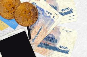 1000 billets de riels cambodgiens et bitcoins dorés avec smartphone et cartes de crédit. concept d'investissement en crypto-monnaie. minage ou commerce de crypto photo