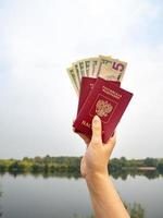 un passeport étranger et des dollars à la main, sur fond de nature. photo