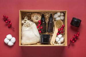 ensemble pour boîte de soins bouteilles d'huile et de crème cosmétiques écologiques, brosse pour le lavage, tampons de coton sur fond rouge cadeau pour petite amie, mère pour célébrer le concept de noël vue de dessus à plat photo