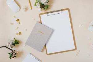 bureau féminin ou blogueur stylisé, bureau. lieu de travail, fleurs blanches d'un pommier, cahier, stylo, trombones et une tablette avec une feuille de papier blanche vierge sur fond beige photo