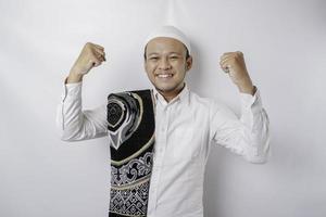 Un jeune homme musulman asiatique heureux avec un tapis de prière sur son épaule montrant une expression réussie isolé par fond blanc photo