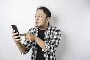 le visage en colère et fou d'un homme asiatique en chemise tartan tout en tenant son téléphone sur fond blanc isolé. photo