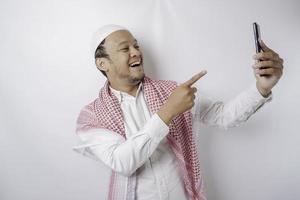 un portrait d'un homme musulman asiatique heureux souriant tout en tenant son téléphone, isolé sur fond blanc photo