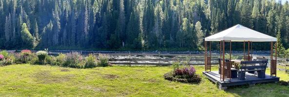 jardin bien entretenu avec un belvédère au bord de la rivière, envahi par une forêt de conifères photo