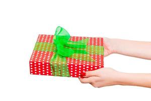 les mains de la femme donnent un noël enveloppé ou d'autres vacances faites à la main dans du papier rouge avec un ruban vert. isolé sur fond blanc, vue de dessus. concept de boîte-cadeau d'action de grâces photo