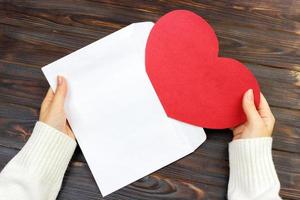 une main de femme tient une enveloppe ouverte et une carte postale sur le bureau en bois, vue de dessus photo