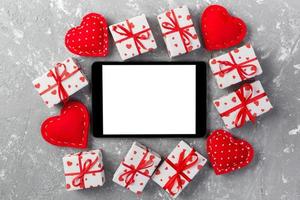 écran vide de tablette numérique avec boîte-cadeau et décor de coeurs sur table en ciment gris. vue de dessus. fond de concept de saint valentin
