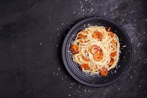 délicieuses pâtes spaghetti aux crevettes et fromage servies dans un bol noir sur fond noir. nouilles italiennes, sauce tomate, légumes et épices recette délicieuse. vue de dessus avec espace de copie photo