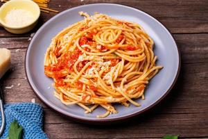 De délicieuses pâtes au fromage spaghetti servies sur une assiette de légumes, sauce tomate italienne et épices disposées sur une table en bois, vue de dessus photo